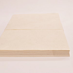 K&ouml;nnte beinhalten: Ein Stapel cremefarbenes Papier, wahrscheinlich Briefpapier oder Notizpapier, wird vor einem wei&szlig;en Hintergrund gezeigt. Das Papier ist ordentlich gestapelt und gebunden, was auf einen Block oder Block von Bl&auml;ttern hindeutet. Das Papier hat eine leicht strukturierte Oberfl&auml;che.
