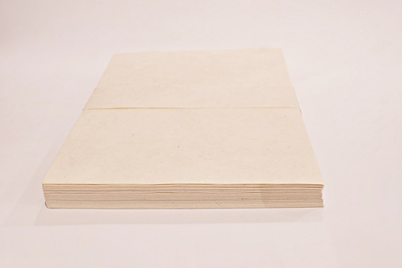 K&ouml;nnte beinhalten: Ein Stapel cremefarbenes Papier, wahrscheinlich Briefpapier oder Notizpapier, wird vor einem wei&szlig;en Hintergrund gezeigt. Das Papier ist ordentlich gestapelt und gebunden, was auf einen Block oder Block von Bl&auml;ttern hindeutet. Das Papier hat eine leicht strukturierte Oberfl&auml;che.