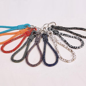 May include: A selection of keyrings in a range of colours: blue, orange, red, black, purple, and white. Each keyring has a looped design with a metal ring for attaching keys. The keyrings are arranged in a fan shape.