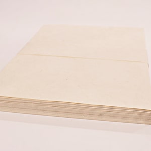 K&ouml;nnte beinhalten: Ein Stapel cremefarbener Papierbl&auml;tter, wahrscheinlich zum Schreiben oder Drucken. Das Papier ist ordentlich gestapelt, mit einer sichtbaren Naht &uuml;ber der Oberseite. Die Kanten des Papiers sind sauber und scharf, was auf ein neues Produkt hindeutet.