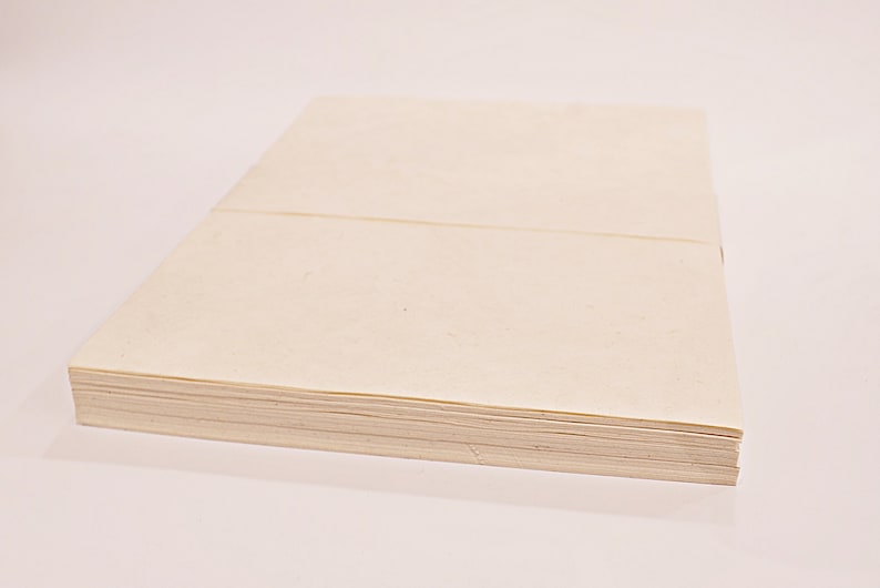 K&ouml;nnte beinhalten: Ein Stapel cremefarbener Papierbl&auml;tter, wahrscheinlich zum Schreiben oder Drucken. Das Papier ist ordentlich gestapelt, mit einer sichtbaren Naht &uuml;ber der Oberseite. Die Kanten des Papiers sind sauber und scharf, was auf ein neues Produkt hindeutet.