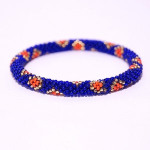 Puede incluir: Un brazalete de cuentas azules y naranjas con un patrón geométrico. El brazalete está hecho de cuentas pequeñas y redondas y tiene un diseño simple y elegante.