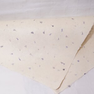 May include: A sheet of handmade paper with embedded purple flower petals. The paper is folded in half and has a rough, textured surface.