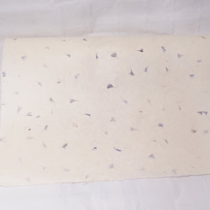 May include: A sheet of white paper with small, scattered purple flower petals embedded in the paper.