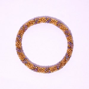 Op de afbeelding: Een geweven armband van paarse en gouden kralen.