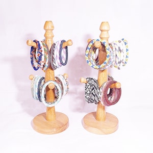 Op de afbeelding: Twee houten standaards met meerdere kleurrijke kralenarmbanden tentoongesteld. De standaards zijn gemaakt van natuurlijk hout en hebben een ronde basis.