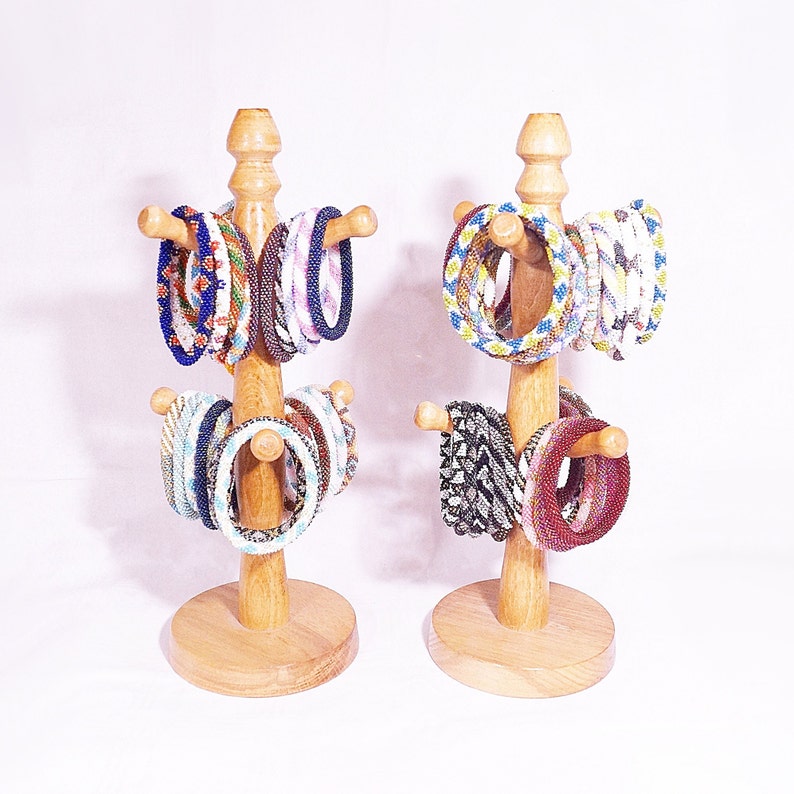 Op de afbeelding: Twee houten standaards met meerdere kleurrijke kralenarmbanden tentoongesteld. De standaards zijn gemaakt van natuurlijk hout en hebben een ronde basis.