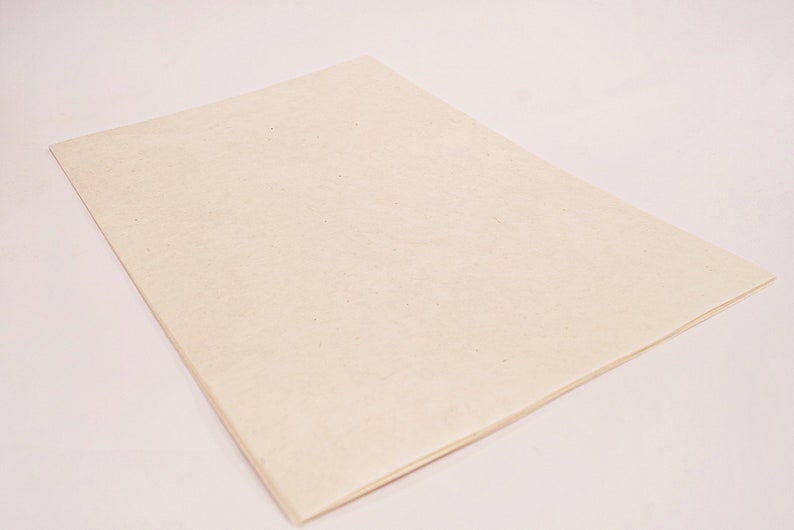 K&ouml;nnte beinhalten: Ein rechteckiges, cremefarbenes Blatt Papier mit leicht strukturierter Oberfl&auml;che. Das Papier liegt flach, die Kanten sind sichtbar, was darauf hindeutet, dass es sich um ein einzelnes Blatt oder einen Papierblock handelt. Der Hintergrund ist hell.