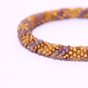 Op de afbeelding: Een close-up van een kralenarmband met een veelkleurig patroon van gouden, bruine en paarse kralen.