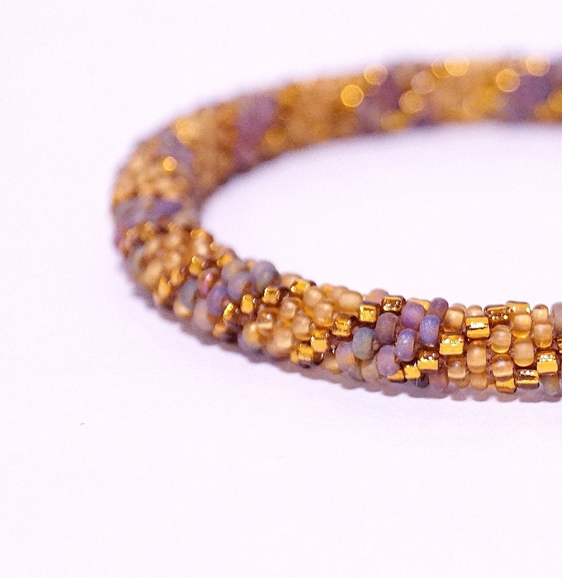 Op de afbeelding: Een close-up van een kralenarmband met een veelkleurig patroon van gouden, bruine en paarse kralen.