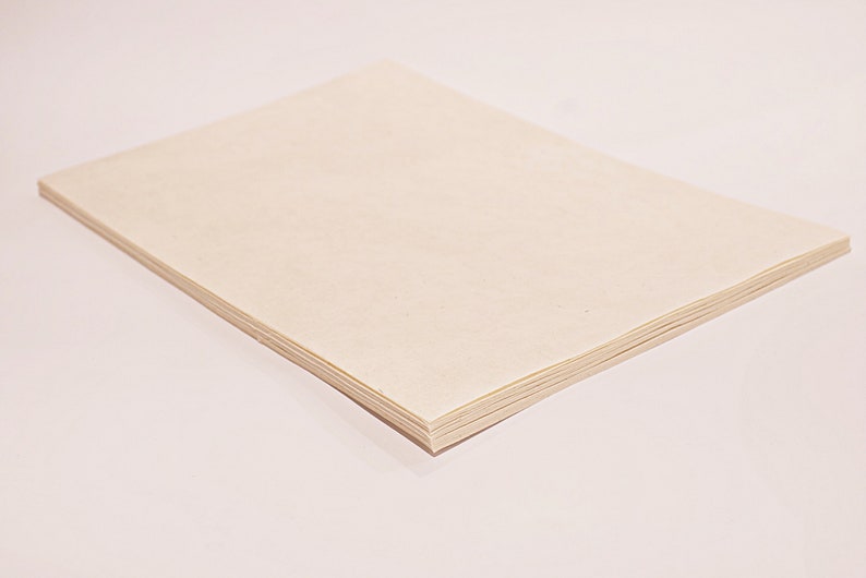 K&ouml;nnte beinhalten: Ein Stapel hellbeige Papierbl&auml;tter, wahrscheinlich zum Zeichnen oder Schreiben, wird auf einer wei&szlig;en Oberfl&auml;che gezeigt. Das Papier hat eine glatte Textur und ein klares, minimalistisches Aussehen. Der Stapel ist rechteckig und scheint unbenutzt.