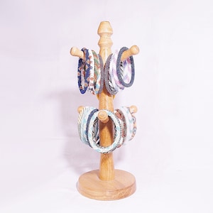 Op de afbeelding: Een houten standaard met meerdere kleurrijke kralenarmbanden in blauw, wit en bruin.