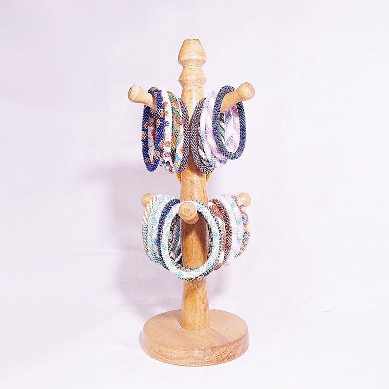 Op de afbeelding: Een houten standaard met meerdere kleurrijke kralenarmbanden in blauw, wit en bruin.