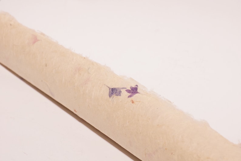 May include: A roll of beige paper with purple and pink pressed flowers embedded in the paper.