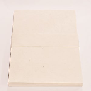 K&ouml;nnte beinhalten: Ein Stapel cremefarbenes Papier, wahrscheinlich Briefpapier oder Notizkarten, wird vor einem wei&szlig;en Hintergrund gezeigt. Das Papier scheint aus einem strukturierten, hochwertigen Material mit sichtbarer Maserung zu bestehen. Der Stapel ist ordentlich angeordnet.