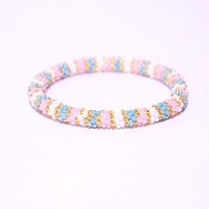 May include: A colourful beaded bracelet with pink, blue and gold beads arranged in a striped pattern.