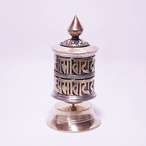 May include: A small, gold and silver prayer wheel with Tibetan script. The wheel is on a stand and has a pointed top.