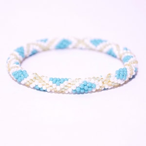 Puede incluir: Un brazalete de cuentas azul, blanco y dorado con un patrón geométrico.