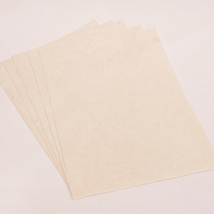 K&ouml;nnte beinhalten: Ein Stapel von f&uuml;nf cremefarbenen, rechteckigen Papierbl&auml;ttern. Das Papier hat eine leicht strukturierte Oberfl&auml;che und ist diagonal angeordnet, f&auml;cherf&ouml;rmig von links unten nach rechts oben. Der Hintergrund ist hell.