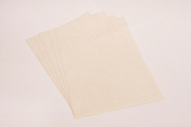 K&ouml;nnte beinhalten: Ein Stapel von f&uuml;nf cremefarbenen, rechteckigen Papierbl&auml;ttern. Das Papier hat eine leicht strukturierte Oberfl&auml;che und ist diagonal angeordnet, f&auml;cherf&ouml;rmig von links unten nach rechts oben. Der Hintergrund ist hell.