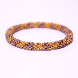 May include: A beaded bracelet featuring a gold and purple colour scheme. The bracelet is made of small, round beads woven together in a spiral pattern.