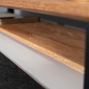 Pu&ograve; includere: Un tavolino da caff&egrave; in legno con un ripiano inferiore. Il tavolo ha una finitura in legno naturale e gambe in metallo nero.