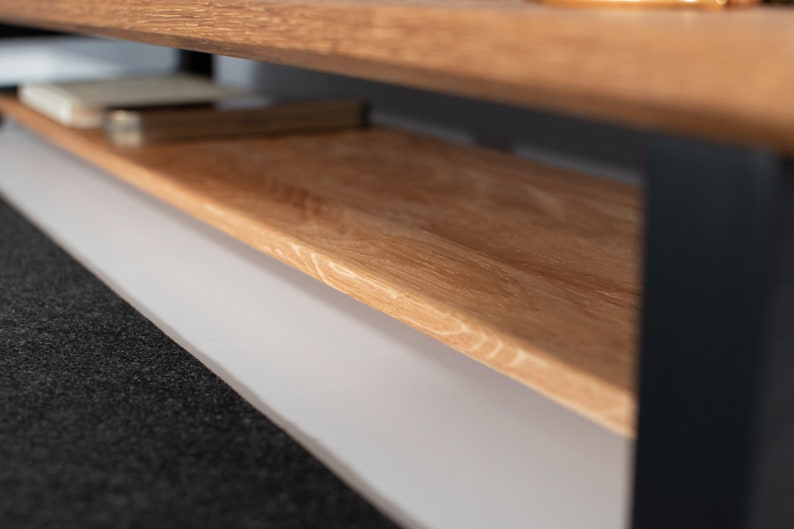 Pu&ograve; includere: Un tavolino da caff&egrave; in legno con un ripiano inferiore. Il tavolo ha una finitura in legno naturale e gambe in metallo nero.