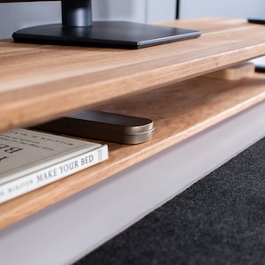 Pu&ograve; includere: Un mobile TV in legno con struttura in metallo nero e un ripiano inferiore. Un libro intitolato "Make Your Bed" &egrave; sul ripiano, insieme a una piccola scatola di metallo.