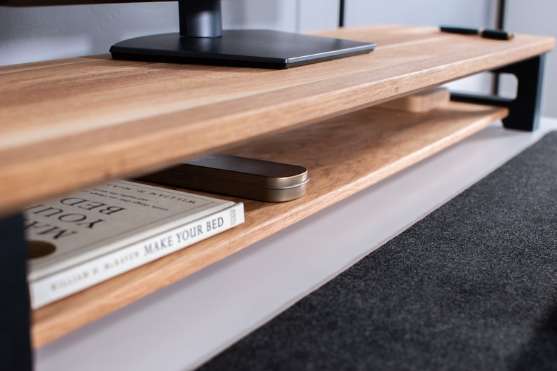 Pu&ograve; includere: Un mobile TV in legno con struttura in metallo nero e un ripiano inferiore. Un libro intitolato "Make Your Bed" &egrave; sul ripiano, insieme a una piccola scatola di metallo.