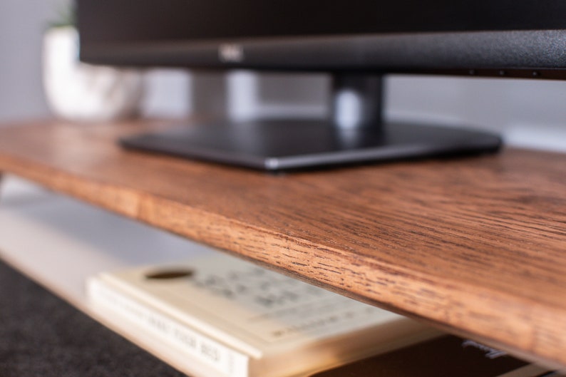 May include: A dark brown wooden TV stand with a flat top surface and a lower shelf. A black flat screen TV is sitting on the top surface.