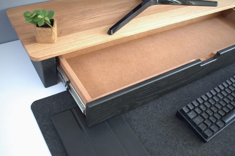K&ouml;nnte beinhalten: Ein schwarzer Holz-Schreibtisch-Aufsatz mit einer Schublade, die offen ist und ein hellbraunes Inneres zeigt. Der Aufsatz steht auf einer schwarzen Filzunterlage. Eine schwarze Tastatur liegt auf der Unterlage.