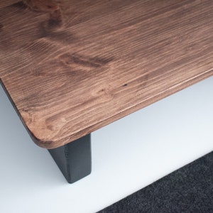 May include: A wooden coffee table with a dark brown stain and black legs. The table top has a natural wood grain pattern.