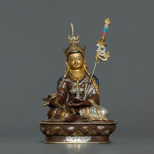 Peut inclure: Une statue dorée et brune d'une figure assise portant une couronne et un sceptre. La figure porte une robe aux détails complexes et tient un petit objet dans sa main. La statue est posée sur un socle avec un motif décoratif.
