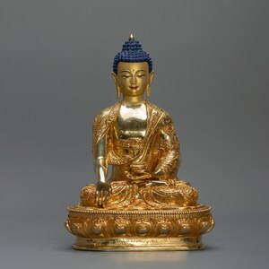 Peut inclure: Une statue dorée de Bouddha assis en position de méditation. La statue porte une couronne bleue et est ornée de détails complexes.