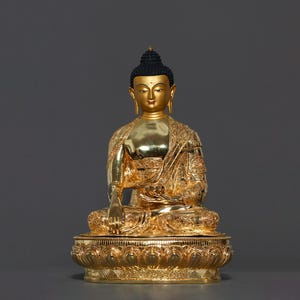 Peut inclure: Une statue dorée de Bouddha assis en position de méditation avec un chignon noir. La statue est sur une base de lotus avec des détails complexes.
