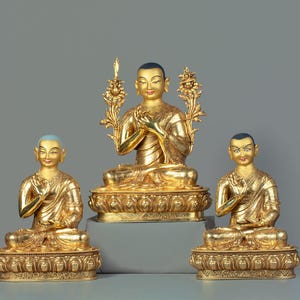 Puede incluir: Tres estatuas doradas de figuras budistas sentadas en posición de meditación. La figura central está sentada en un trono con un diseño floral. Las figuras llevan todas ropas tradicionales y tienen expresiones serenas.
