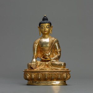 Peut inclure: Une statue dorée de Bouddha assis en position de méditation. La statue est ornée de sculptures complexes et porte une perruque noire.
