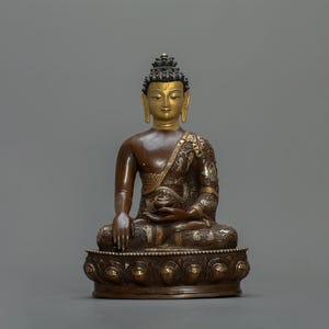 Peut inclure: Une statue en métal doré et brun de Bouddha assis en position de méditation. La statue est ornée de sculptures complexes et est posée sur une base en forme de lotus.