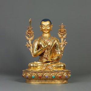 Puede incluir: Una estatua dorada de un Buda sentado con una corona de joyas y decoraciones ornamentadas. El Buda sostiene un gesto de mano frente a su pecho.