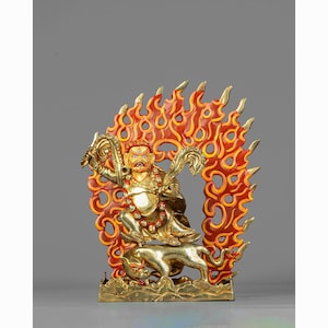 May include: A gold-colored statue of a deity with a red and orange flame-like halo behind it. The deity is sitting on a lion with a fierce expression and holding a weapon in one hand.