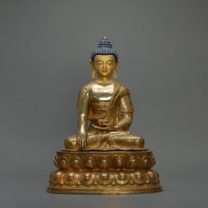 Peut inclure: Une statue dorée de Bouddha assis en position de méditation sur une base de lotus. La statue est en métal et présente un design détaillé.