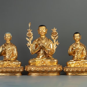 Puede incluir: Tres estatuas doradas de figuras budistas sentadas en una postura meditativa. Las estatuas están sobre bases ornamentadas y tienen un diseño tradicional.