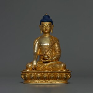 Peut inclure: Une statue dorée de Bouddha assis en position de méditation. La statue est ornée de sculptures complexes et porte une couronne bleue.