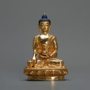 Peut inclure: Une statue dorée de Bouddha assis en position de méditation. La statue est ornée de sculptures complexes et porte une couronne bleue.