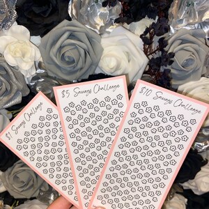 May include: Three printable savings challenge trackers with pink borders and black flower designs. The trackers are labeled "$1 Savings Challenge", "$5 Savings Challenge", and "$10 Savings Challenge".