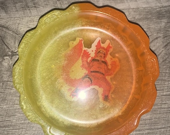 Può includere: Un vassoio rotondo in resina con bordo smerlato, con una sfumatura da giallo ad arancione. Il vassoio ha un personaggio dei cartoni animati al centro. Il vassoio è su una superficie di legno. Questo vassoio è adatto per l'arredamento della casa.