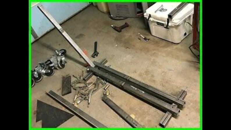May include: A metal frame with wheels and a metal bar attached to it. The frame is made of square tubing and the bar is made of round tubing. The frame is sitting on a concrete floor.