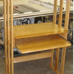 May include: A light-colored wooden desk with a top shelf, a middle shelf, and a pull-out keyboard tray. The desk has a simple, functional design with vertical supports and a natural wood finish. The desk is approximately 48 inches tall.