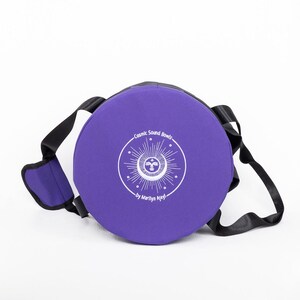 Pu&ograve; includere: Borsa rotonda viola con una tracolla nera e un logo ricamato bianco che dice "Cosmic Sound Bowls by Marilyn Mlyni".
