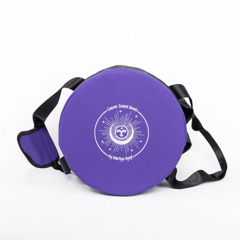 Pu&ograve; includere: Borsa rotonda viola con una tracolla nera e un logo ricamato bianco che dice "Cosmic Sound Bowls by Marilyn Mlyni".